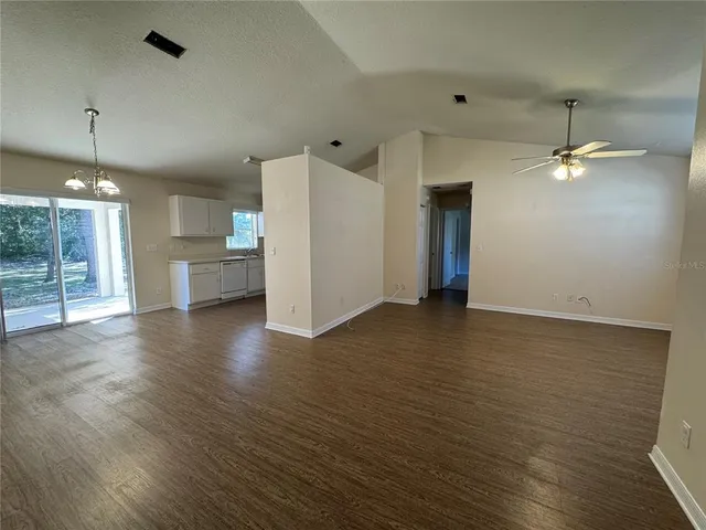 an empty room with wooden floor and kitchen view