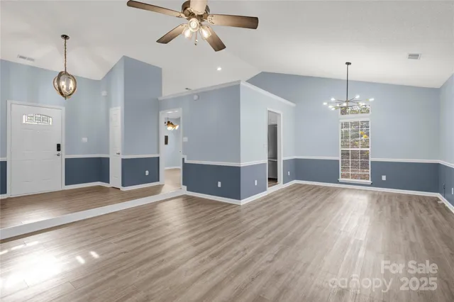 an empty room with wooden floor chandelier and windows