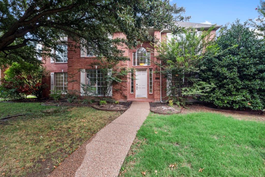 a view of a brick house with a big yard and large tree