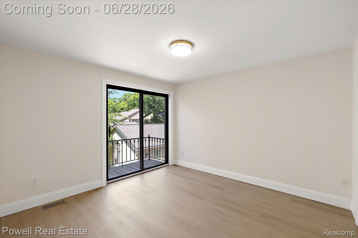 1447 Ravineview Court, Unit C12 Bloomfield Hills, MI 48304 - Photo 37 of 49 Room featuring a sliding glass door opening to a private balcony with black metal railings, neutral wall paint, light wood-finish flooring, and a flush-mount ceiling light fixture