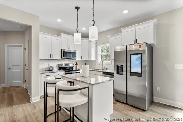 a kitchen with a refrigerator a microwave a stove and white cabinets with wooden floor