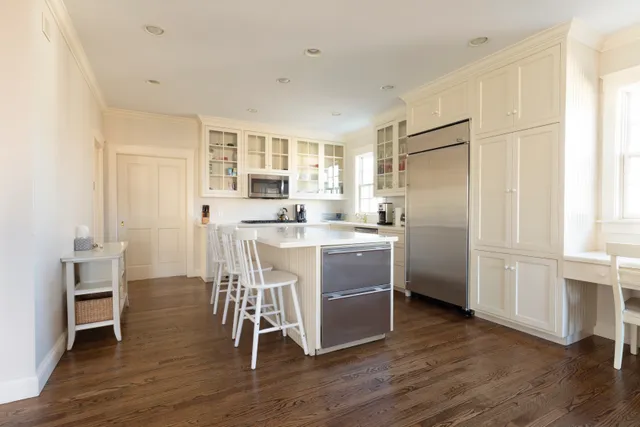 a kitchen with stainless steel appliances a stove a sink dishwasher a refrigerator white cabinets and wooden floor next to a window