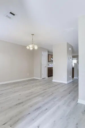 a view of empty room with wooden floor and kitchen