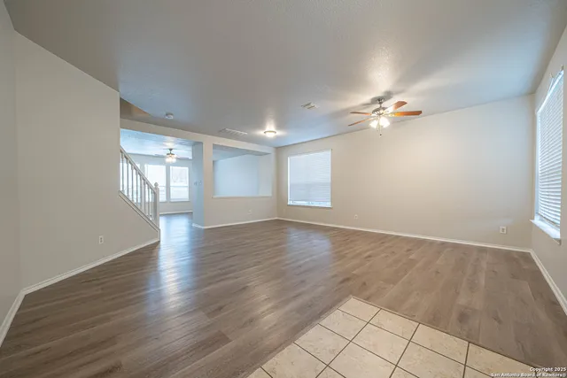 an empty room with wooden floor chandelier fan and windows