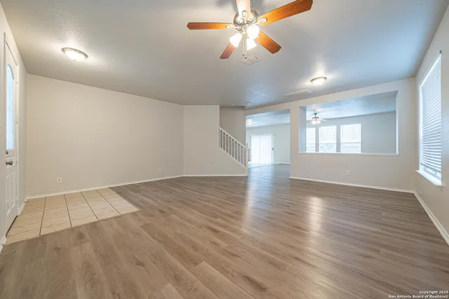 an empty room with wooden floor chandelier fan and windows