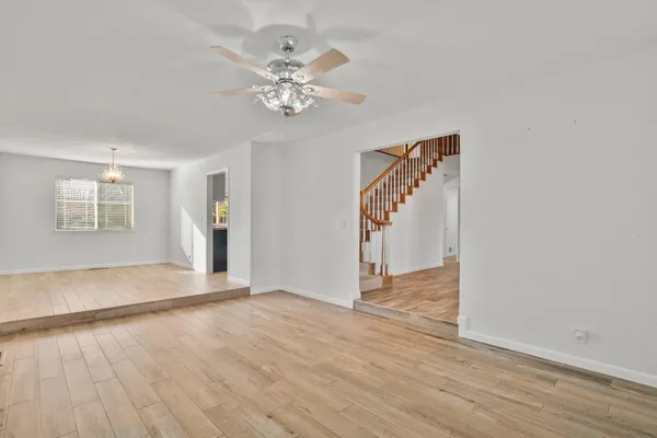 a view of an empty room with chandelier fan and wooden floor