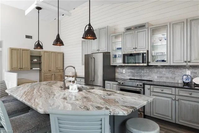 a kitchen with stainless steel appliances granite countertop a stove a sink a microwave a refrigerator and white cabinets with wooden floor