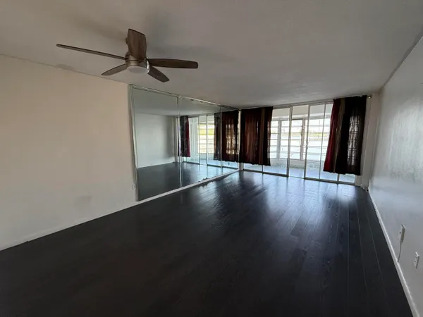 an empty room with wooden floor fan and windows