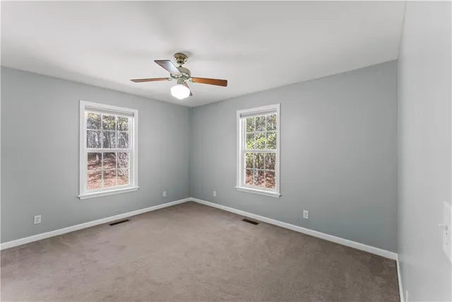 an empty room with chandelier fan and windows