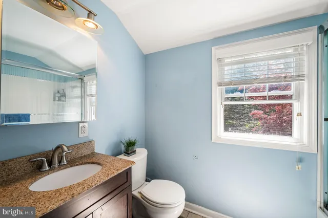 a bathroom with a granite countertop sink toilet a mirror and a window