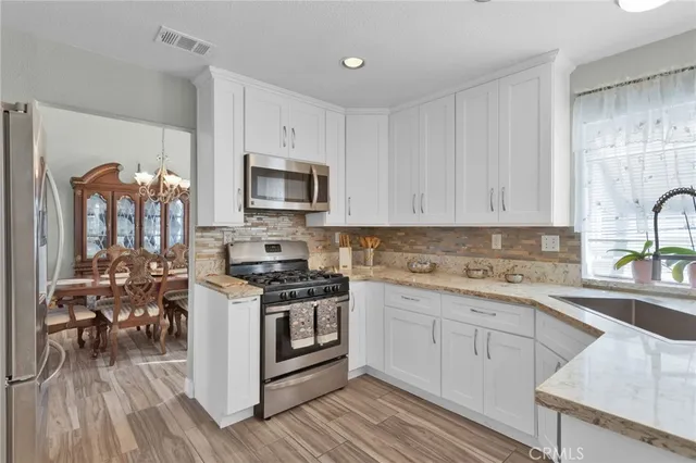 a kitchen with stainless steel appliances granite countertop a stove top oven a sink dishwasher and white cabinets with wooden floor