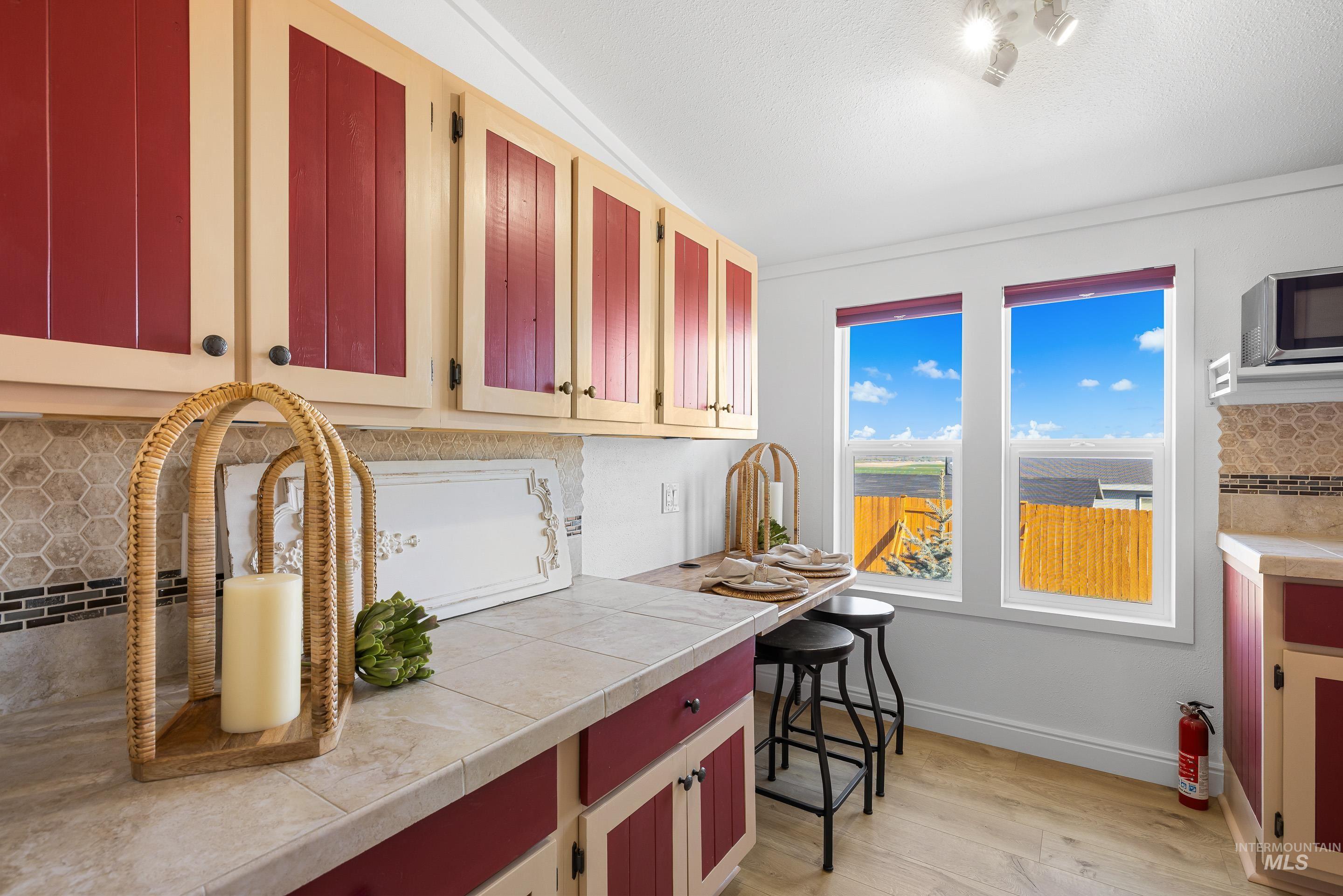 2427 Northside Road Homedale, ID 83628 - Photo 14 of 49 Kitchen featuring light countertops, light wood-style floors, tasteful backsplash, stainless steel microwave, and red cabinetry