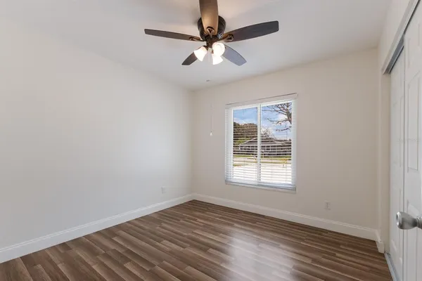 an empty room with wooden floor chandelier fan and windows