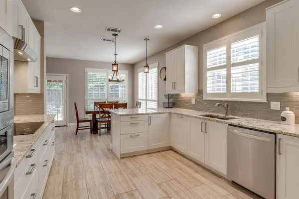 a large white kitchen with granite countertop a stove a sink dishwasher a dining table and chairs with wooden floor