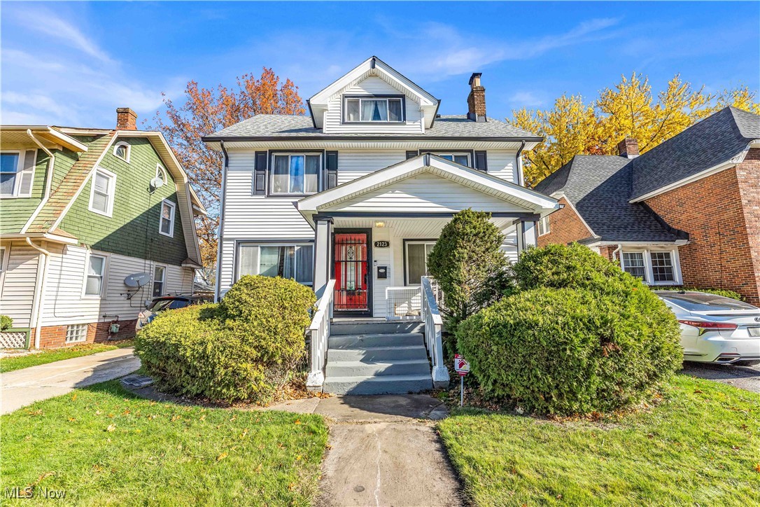 American foursquare style home with a front lawn, a chimney, covered porch, and a shingled roof