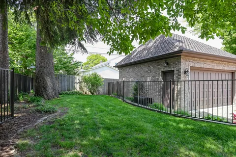 a small barn in front of a yard with wooden fence and a large tree