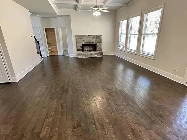 an empty room with wooden floor fireplace and windows