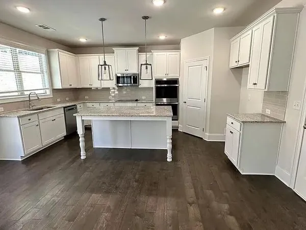 a kitchen with stainless steel appliances granite countertop a refrigerator a sink dishwasher a stove and white cabinets with wooden floor