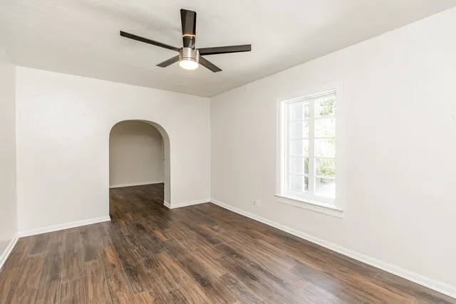 an empty room with wooden floor fan and windows