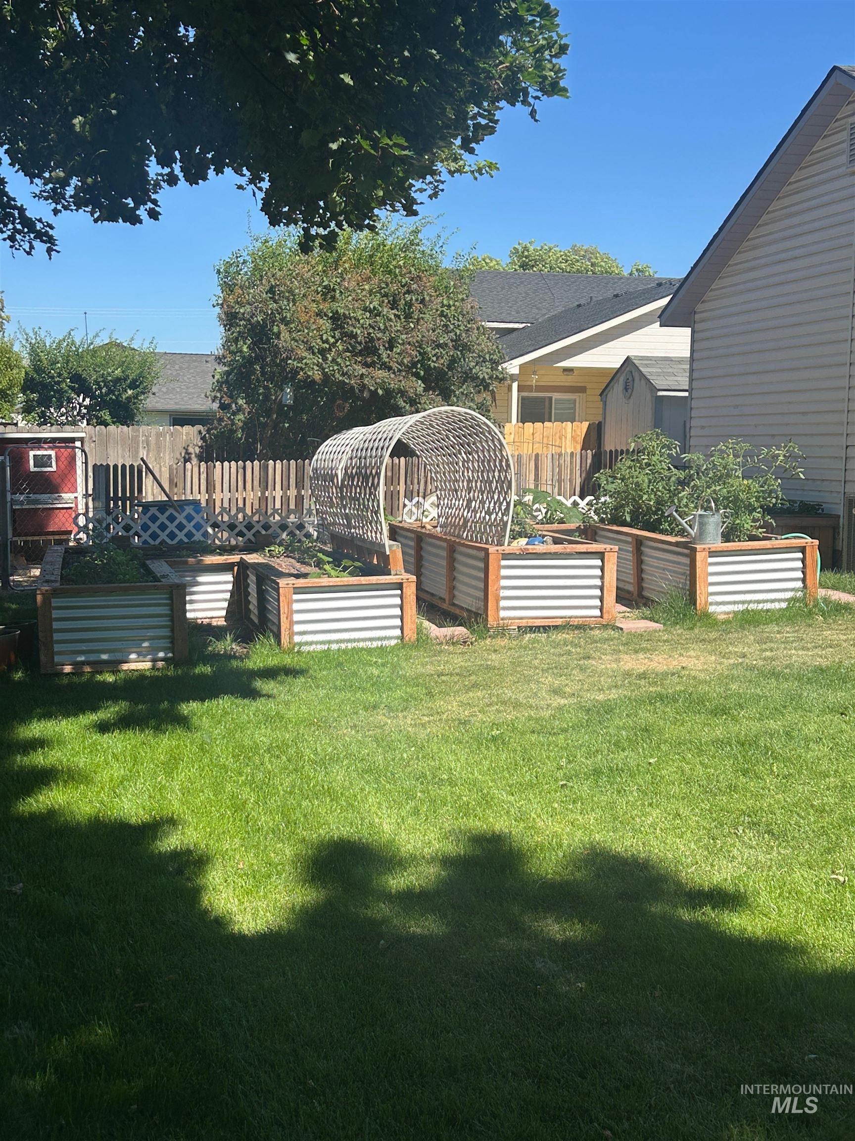 1444 East Doberman Street Meridian, ID 83642 - Photo 29 of 31 Grassy backyard featuring multiple raised garden beds with wood and corrugated metal construction, a garden tunnel, and a wooden fence perimeter