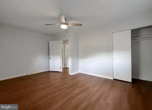 a view of an empty room with wooden floor and a ceiling fan