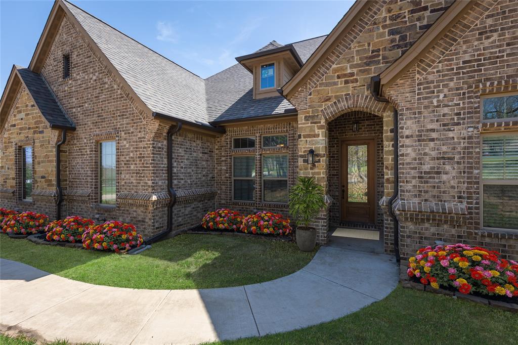 143 Wrigley Drive Springtown, TX 76082 - Photo 11 of 40 Virtually Staged - Brick exterior with arched entryway, wood-finish front door with glass insert, gabled roofline, multiple windows, and a curved concrete walkway