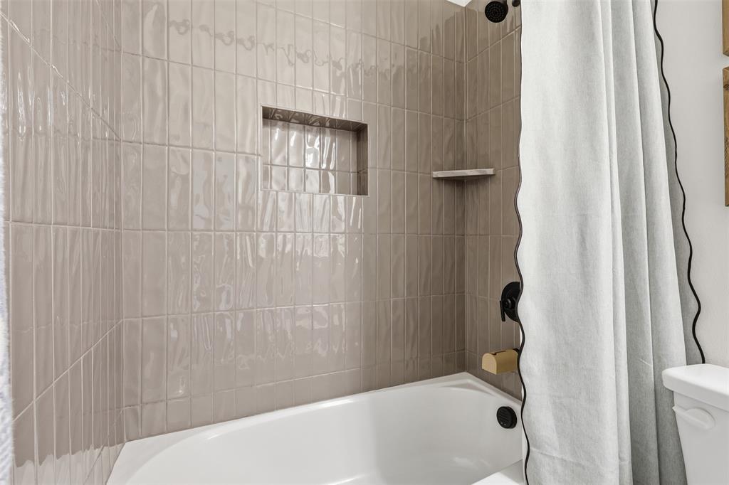 15413 Short Rdg Lane Fort Worth, TX 76008 - Photo 23 of 39 White bathtub with light gray vertical subway tile surround, featuring a built-in shower niche and a corner shelf