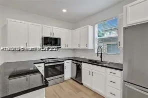 a kitchen with granite countertop a sink stainless steel appliances and white cabinets
