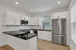 a kitchen with granite countertop a sink a stove a refrigerator and white cabinets