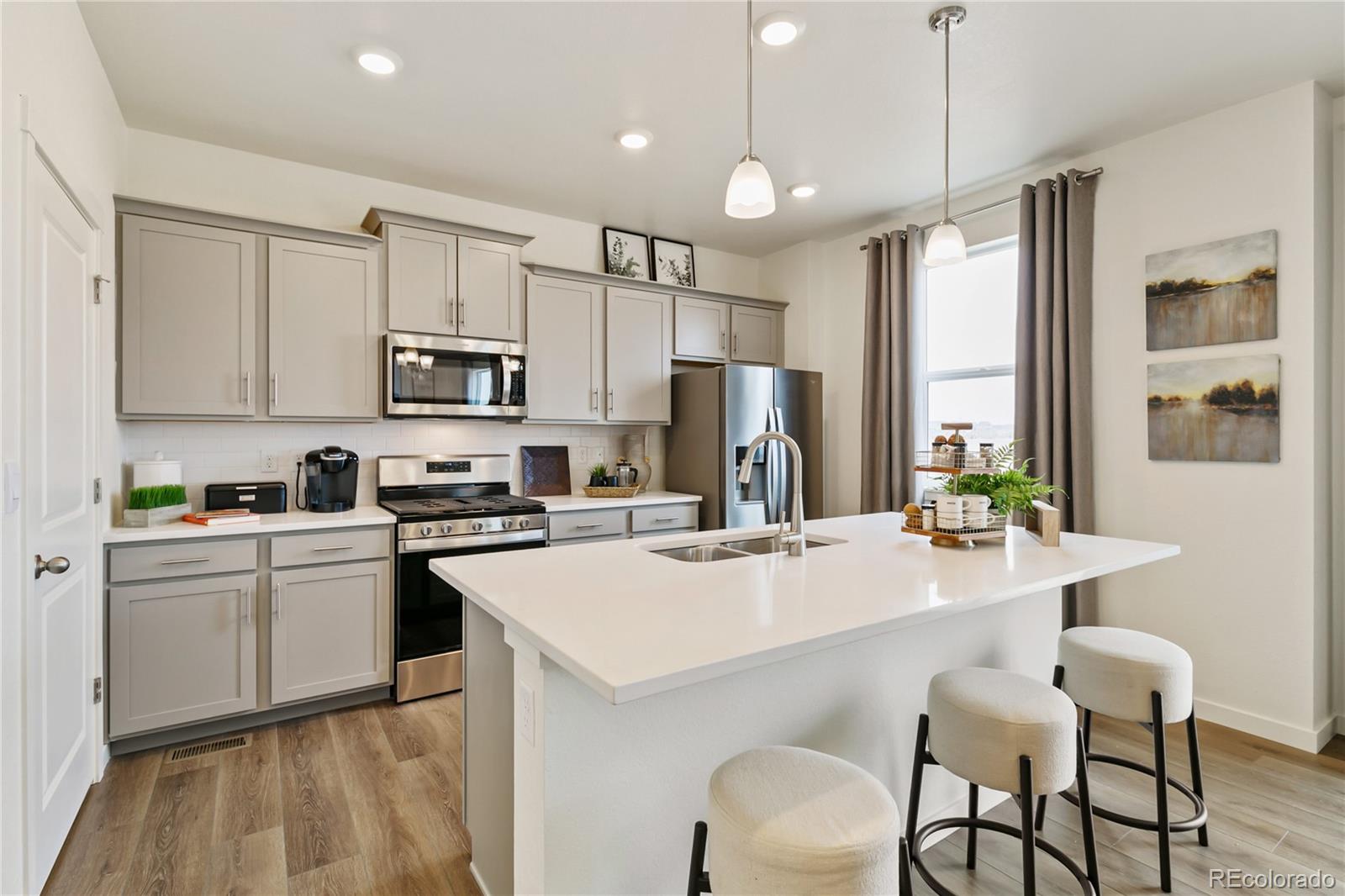 9935 Ceylon Court Commerce City, CO 80022 - Photo 10 of 44 a kitchen with a sink a stove a refrigerator and white cabinets with wooden floor