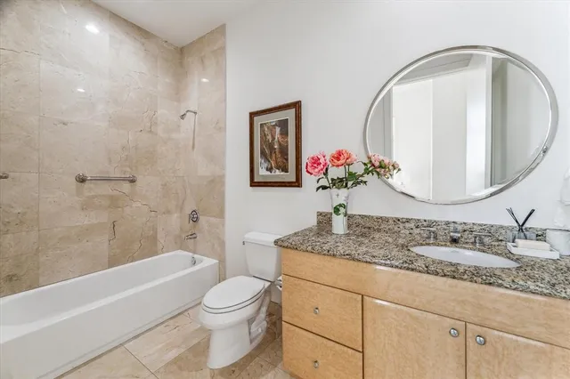 a bathroom with a granite countertop sink a toilet a mirror a vanity and bathtub