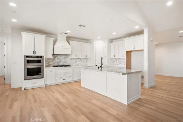a kitchen with stainless steel appliances kitchen island granite countertop a stove a sink a refrigerator and white cabinets with wooden floor