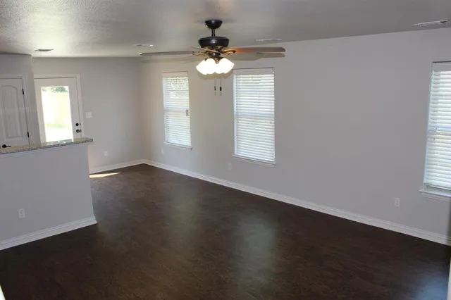 an empty room with wooden floor chandelier fan and windows