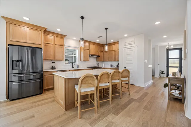 a kitchen with stainless steel appliances kitchen island granite countertop a refrigerator a stove a sink and a dining table with wooden floor