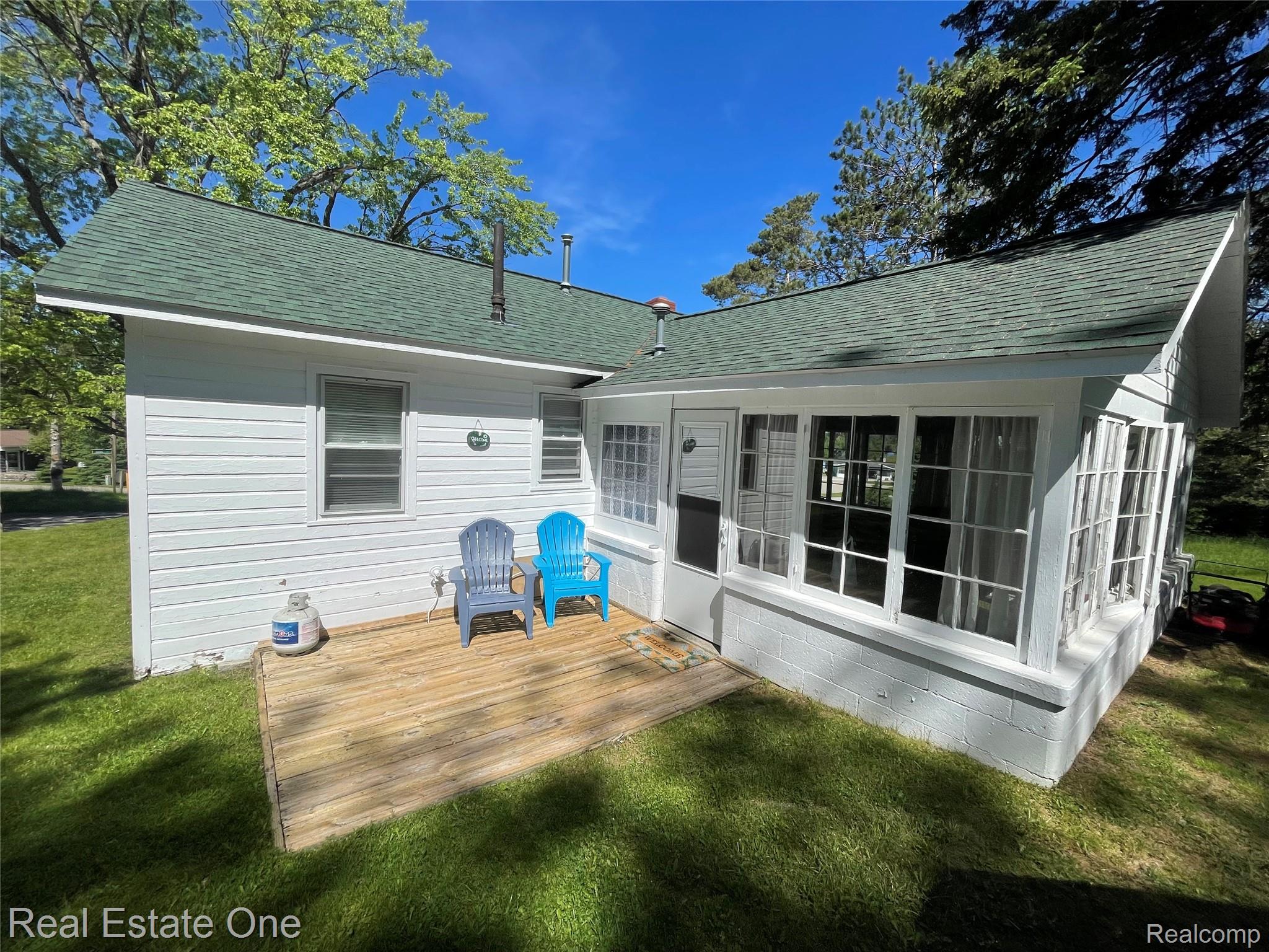 4160 Hawk Road Lincoln, MI 48742 - Photo 11 of 48 Exterior featuring white horizontal siding, a green asphalt shingle roof, a sunroom with multiple windows, and a wood deck