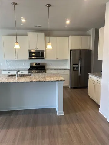 a kitchen with stainless steel appliances granite countertop a refrigerator a sink dishwasher a stove and a wooden floor