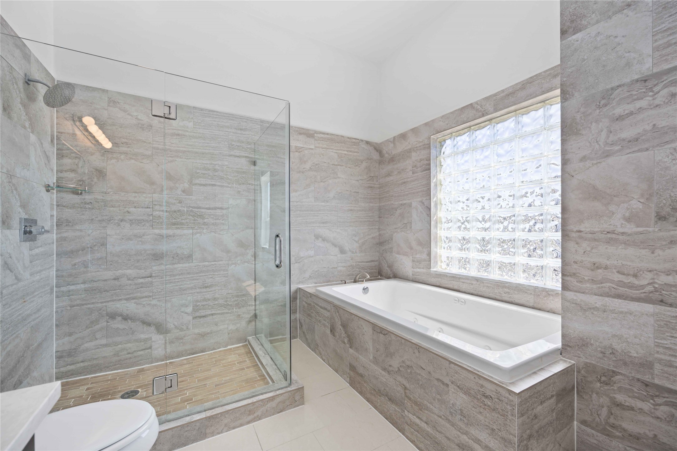 2211 Detering Street, Unit B Houston, TX 77007 - Photo 17 of 22 The primary bathroom features a spacious glass-enclosed shower and a large jetted tub. It has modern tile walls and a glass block window for natural light and privacy.