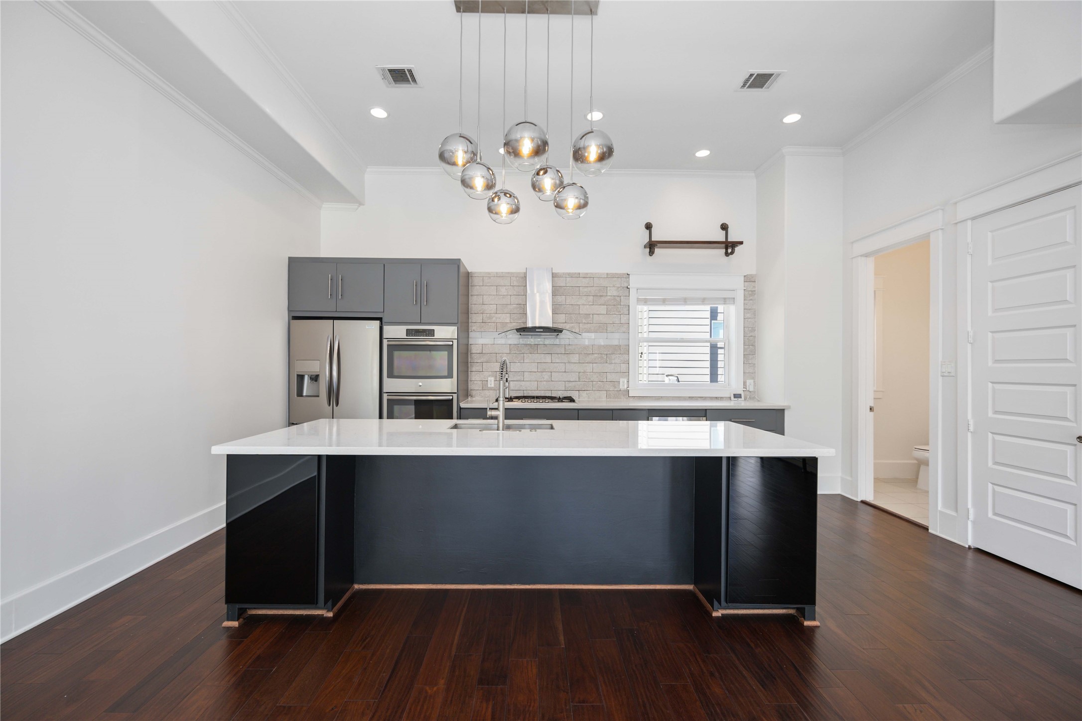 2211 Detering Street, Unit B Houston, TX 77007 - Photo 9 of 22 Modern kitchen with sleek, dark cabinetry and stainless steel appliances. Features a large white island with a built-in sink and elegant pendant lighting.