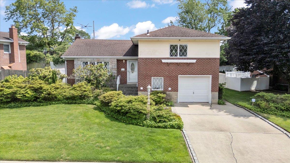 Split level home with brick siding, a garage, concrete driveway, a chimney, and a shingled roof