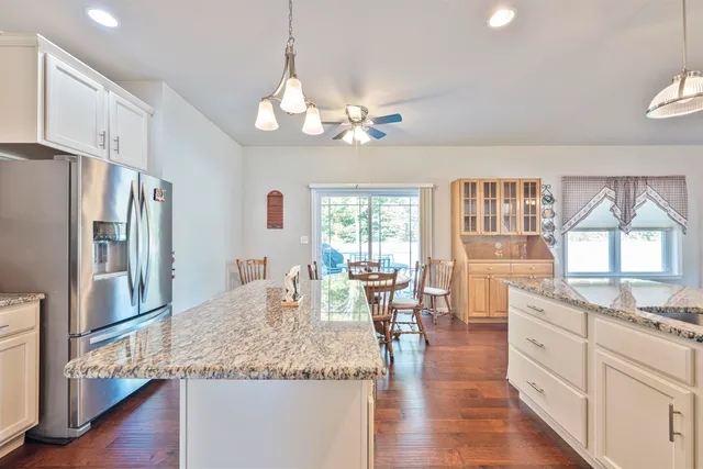 a kitchen with stainless steel appliances granite countertop a refrigerator a stove top oven a sink dishwasher and white cabinets with wooden floor