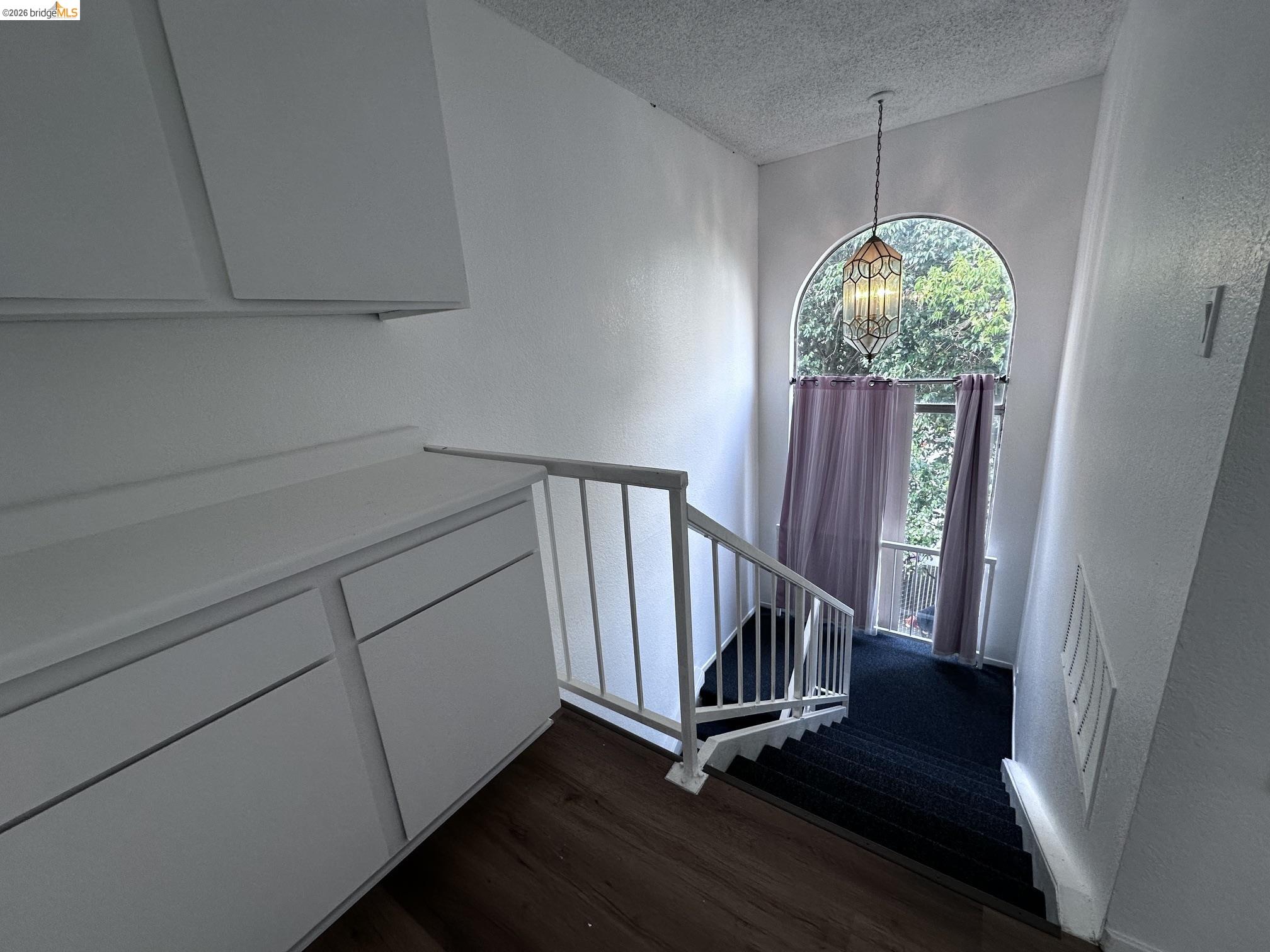 2121 Vale Road, Unit 17 San Pablo, CA 94806 - Photo 10 of 17 Arched window with decorative pendant lighting, white painted railings, built-in cabinetry, wood-finish flooring, and carpeted stairs
