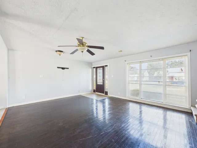 an empty room with wooden floor fan and windows