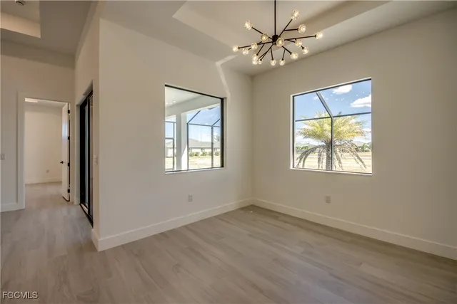 an empty room with wooden floor chandelier fan and windows