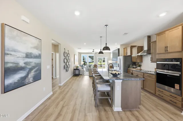 a kitchen with stainless steel appliances kitchen island granite countertop a stove a refrigerator a sink a dining table and chairs with wooden floor