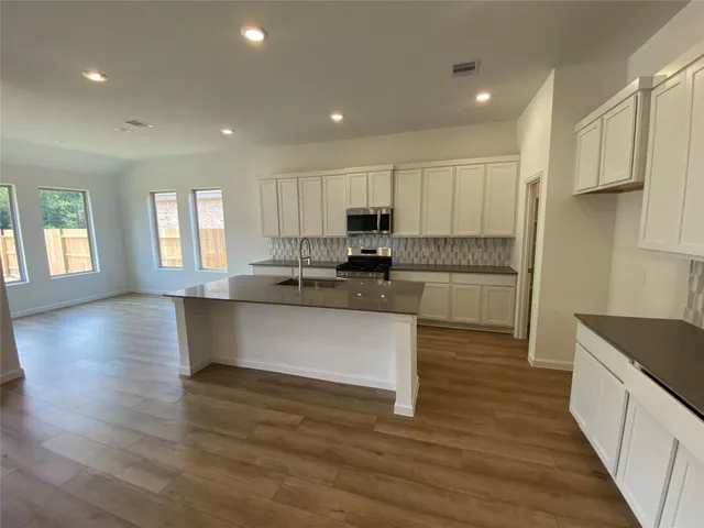 a kitchen with stainless steel appliances granite countertop a stove a sink and white cabinets with wooden floor