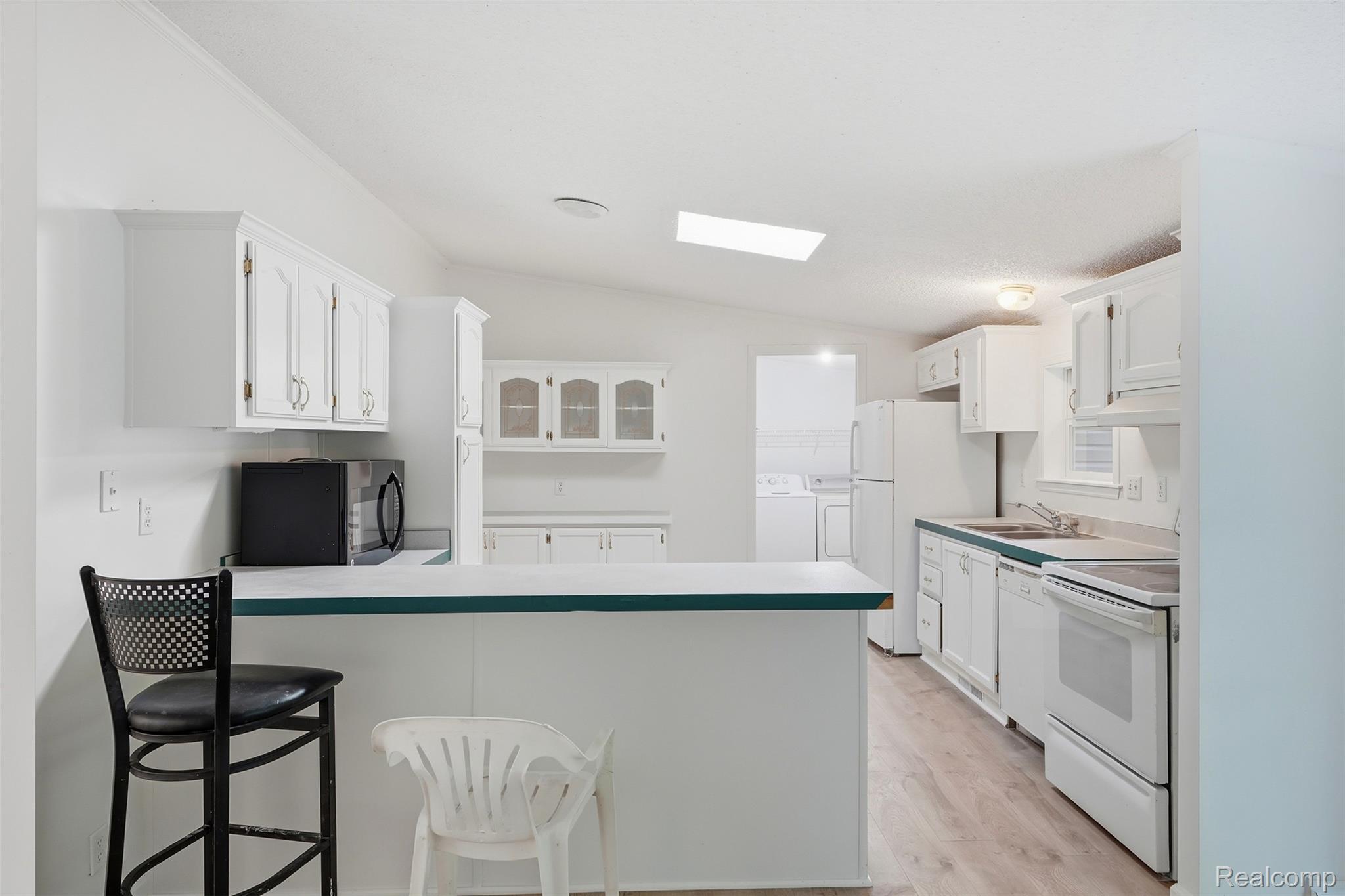 3432 Stanton Road Oxford, MI 48371 - Photo 12 of 48 Bright kitchen featuring white cabinetry, a breakfast bar, white appliances, a skylight, and wood-finish flooring