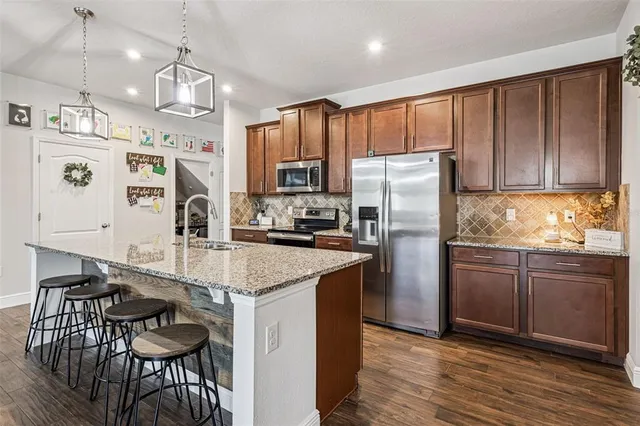 a kitchen with stainless steel appliances granite countertop a refrigerator a stove a sink dishwasher a dining table and chairs with wooden floor
