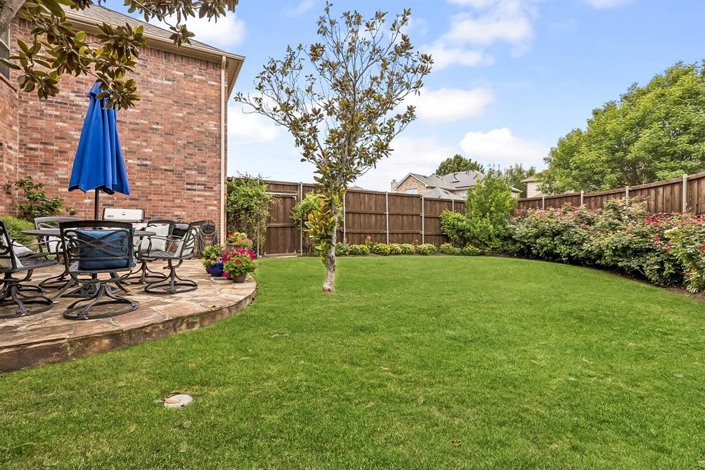 960 Remuda Road Frisco, TX 75033 - Photo 31 of 39 Expansive backyard featuring a stone patio, vibrant green lawn, mature trees, and a perimeter wood fence