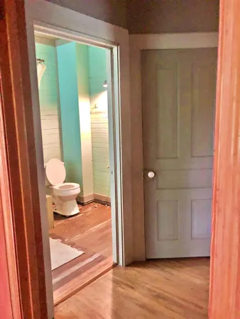 a view of a hallway with wooden floor and a bathroom