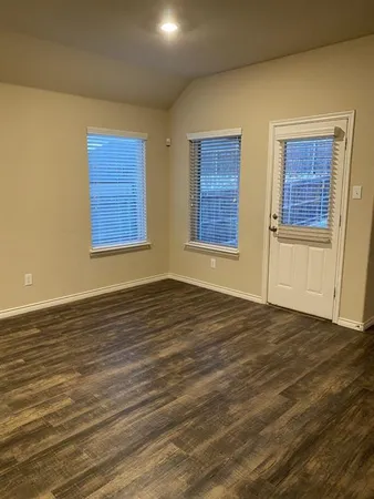 a view of an empty room with wooden floor and windows